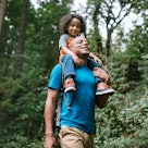 A dad with his child on his shoulders goes on a walk in a forest for his mental health.