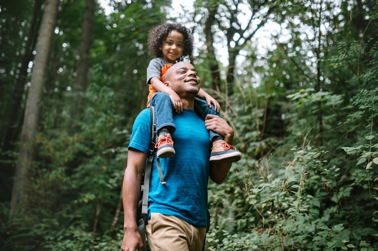 A dad with his child on his shoulders goes on a walk in a forest for his mental health.