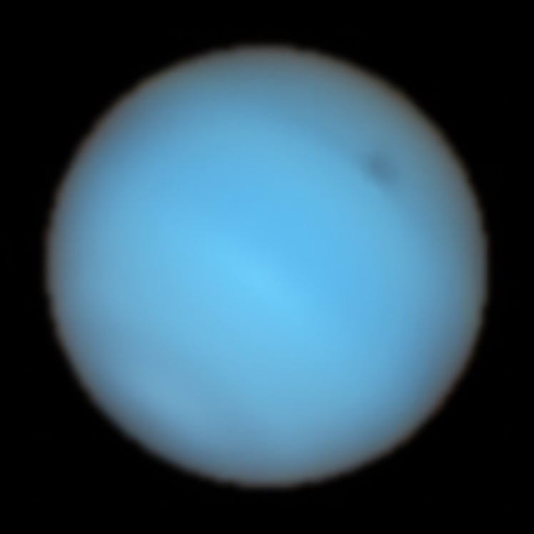Neptune has a hazy appearance, but on the top right, there is a spot darker than its surroundings. 