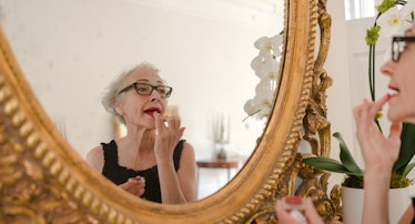 the makeup artist Rose-Marie Swift putting on lipstick in a gilt mirror