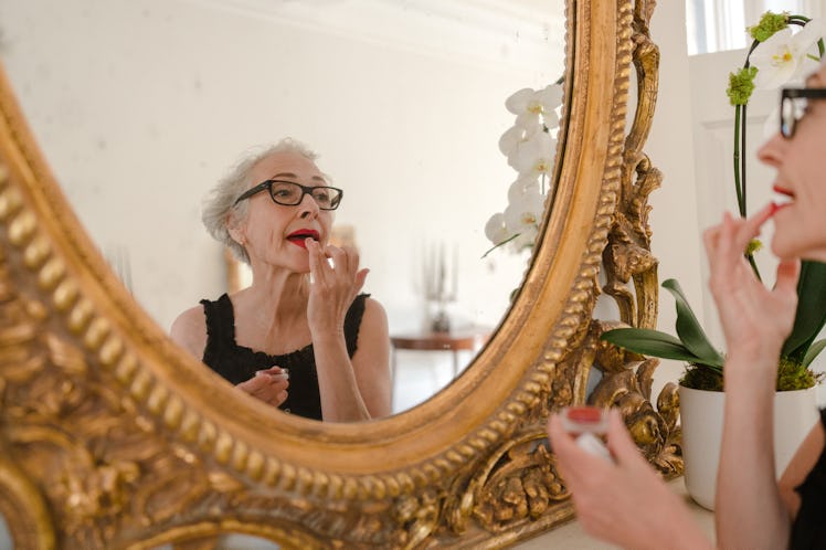 the makeup artist Rose-Marie Swift putting on lipstick in a gilt mirror