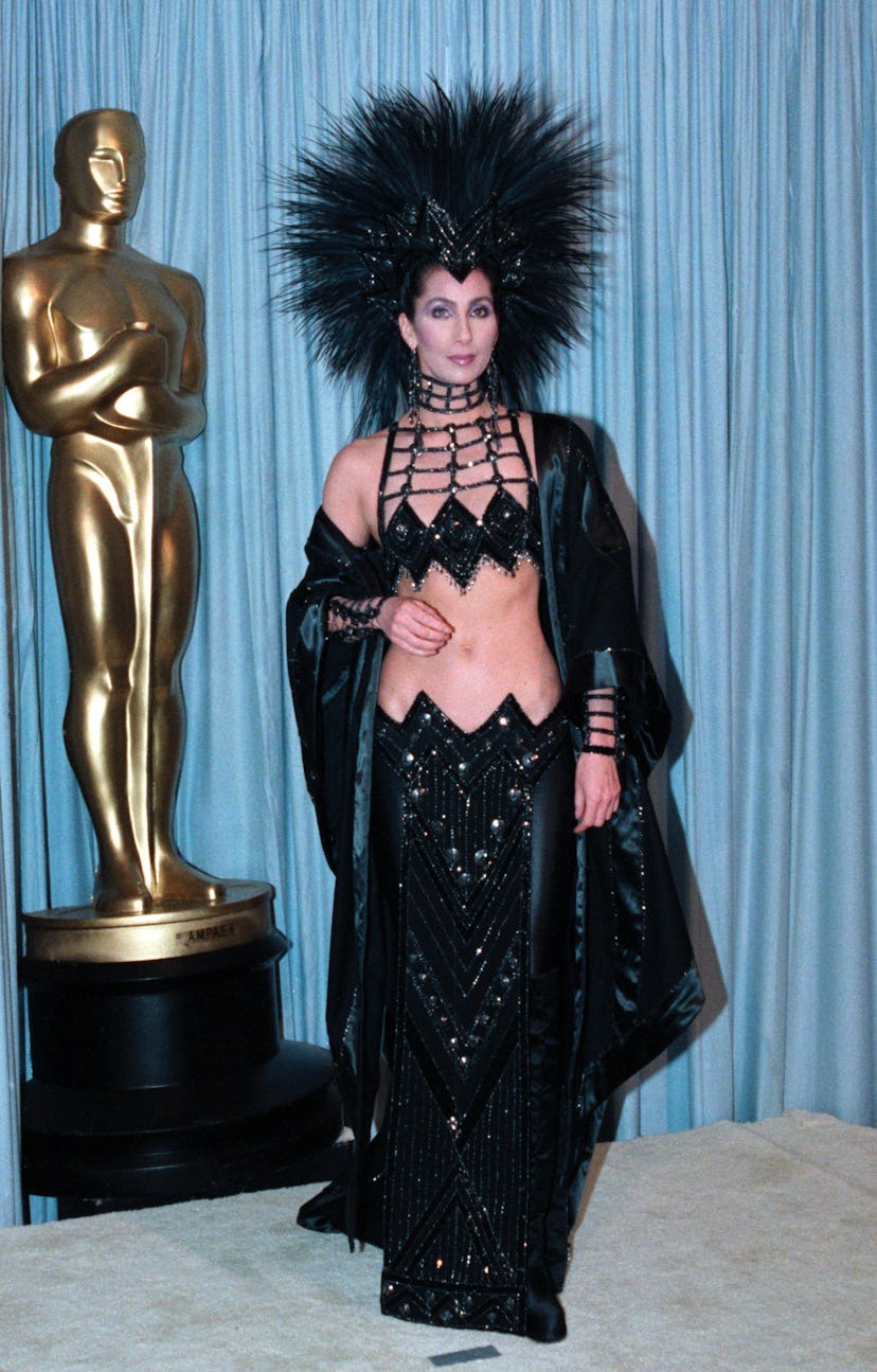 Cher wears a beaded bra top, low-rise skirt, and headdress at the Oscars. 