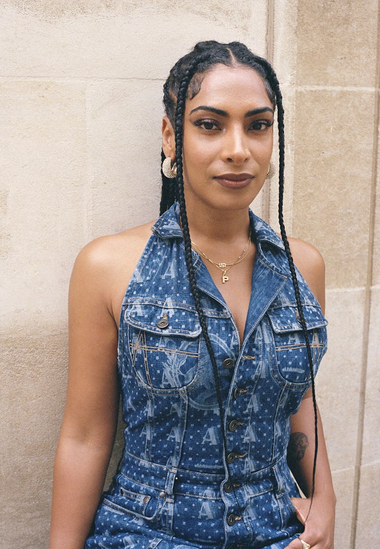 Designer Priya Ahluwalia wears a denim jumpsuit, gold earrings, gold necklace and gold ring.