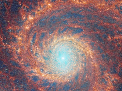 A large spiral galaxy takes up the entirety of the image. The core is mostly bright white, but there...