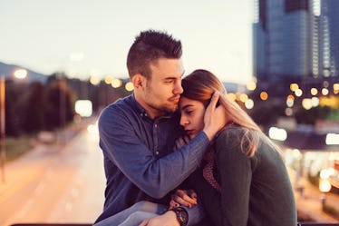 Sad woman resting her head on a man's shoulder outside near cityscape