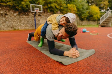 A man doing planks outside on a basketball court with his child on his back.