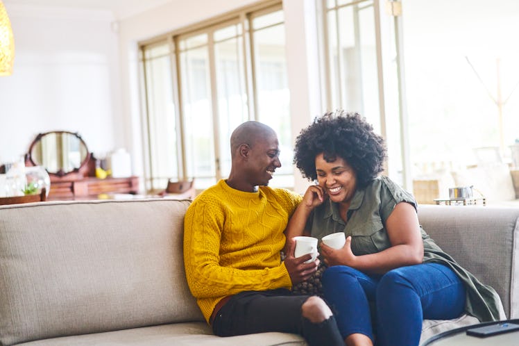 Husband and wife sitting on the couch with coffee, having a happy conversation and laughing