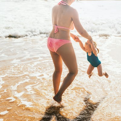 A woman in a bathing suit spins her child at the beach.