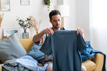 Middle aged man folding t-shirt while sitting on the couch