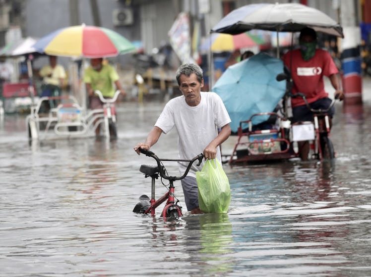 a filipino man walking his bike through knee deep water with several bicycle rickshaw drivers in the...