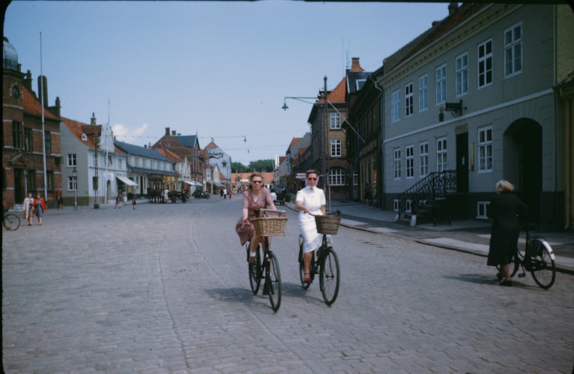 Two women ride their bikes down a cobblestone road in Copenhagen, Denmark in 1946