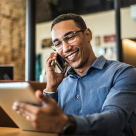 Man networking over the phone as he stares at a tablet and smiles