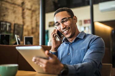 Man networking over the phone as he stares at a tablet and smiles