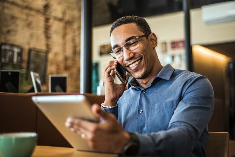 Man networking over the phone as he stares at a tablet and smiles