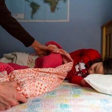 A mom tucks a child into bed.