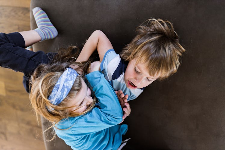 Two siblings fighting, wrestling aggressively on a couch.