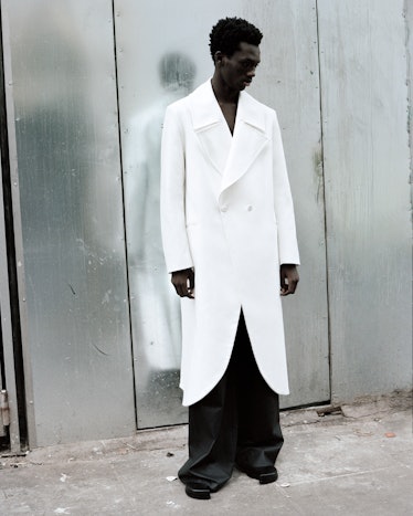 A model wears a white longline coat and black baggy trousers by Erin Esh