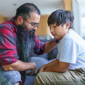 A dad having a serious conversation with his son, putting his hand on his son's shoulder.