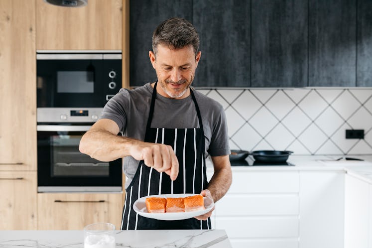 A man seasoning salmon before cooking it in his kitchen at home.