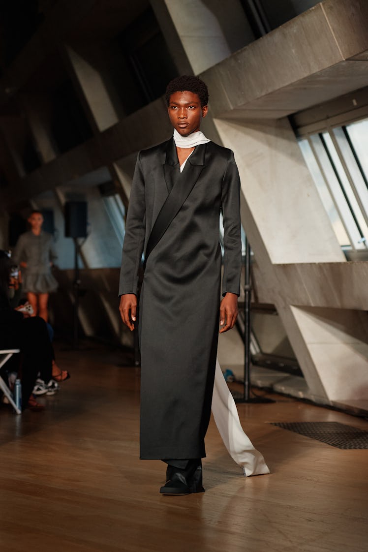 A model wears a black longline coat and white silk scarf by Erin Esh
