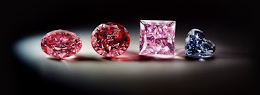 Four diamonds sit on a surface, illuminated from above. The first two are round and rich in color, t...