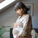 A pregnant woman looks down at her belly anxiously.