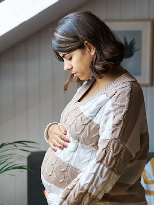 A pregnant woman looks down at her belly anxiously.