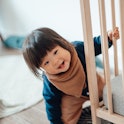 A smiling toddler peeks around the corner of their crib mattress.