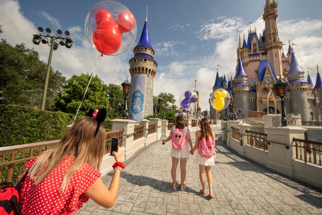Girls take pictures at Disney World's Magic Kingdom holding Mickey balloons.