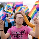A trans person in a shirt that says "gender free" waving trans and rainbow flags among a crowd of LG...