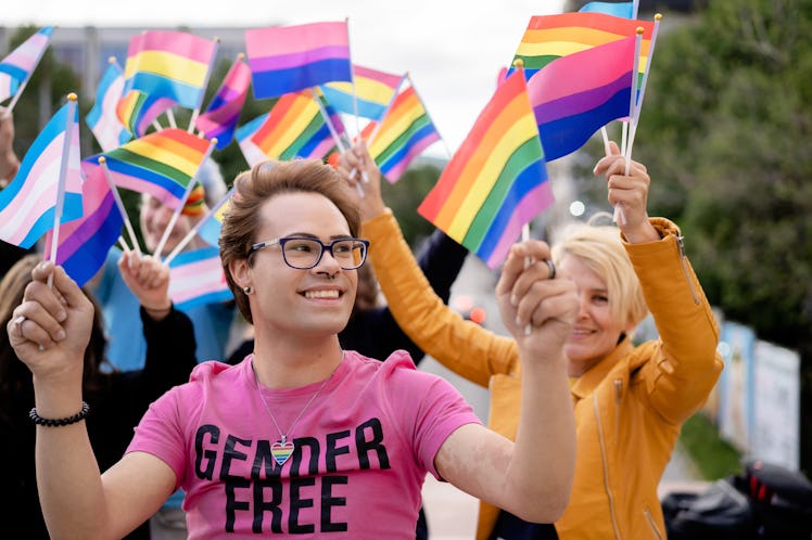A trans person in a shirt that says "gender free" waving trans and rainbow flags among a crowd of LG...