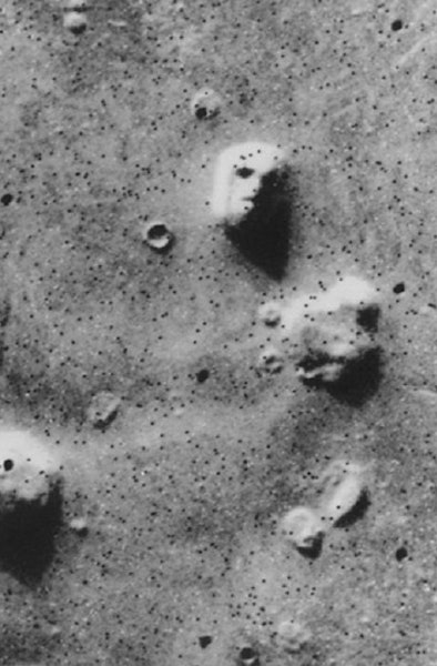 aerial grayscale photo of rock formations on Mars, one of which looks like a face