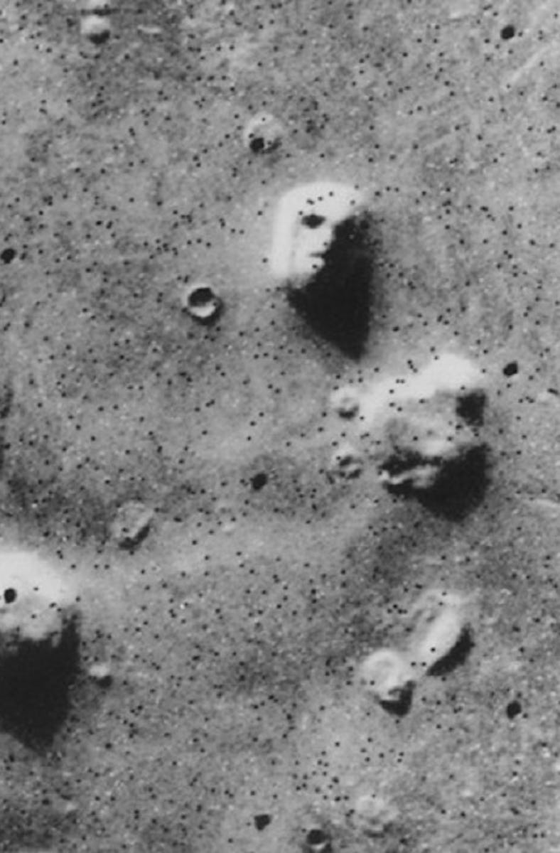 aerial grayscale photo of rock formations on Mars, one of which looks like a face