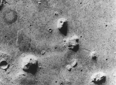 aerial grayscale photo of rock formations on Mars, one of which looks like a face