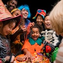 A family trick-or-treating on Halloween, grabbing candy from a bowl being held by their neighbor in ...
