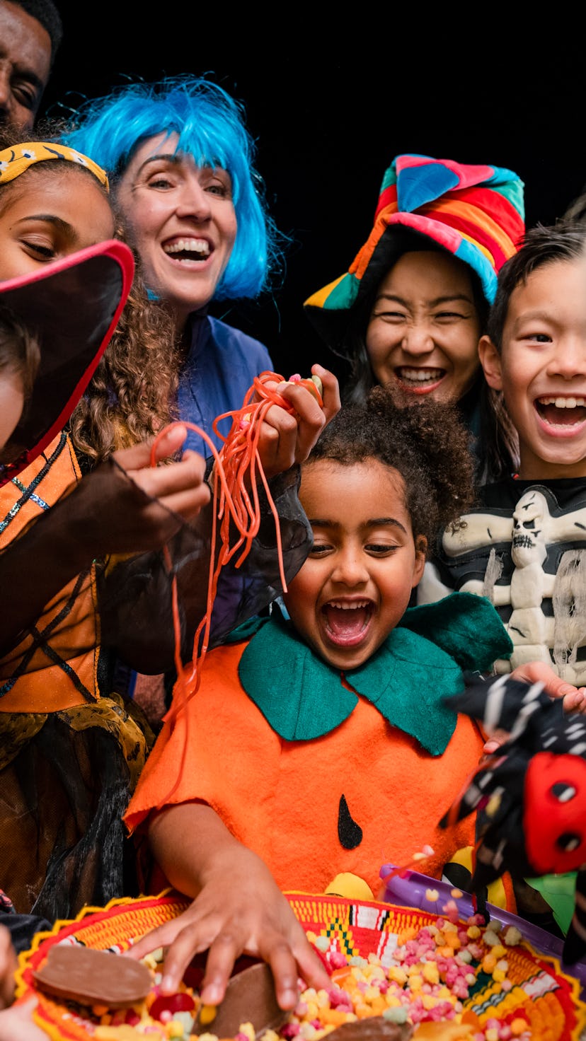 A family trick-or-treating on Halloween, grabbing candy from a bowl being held by their neighbor in ...