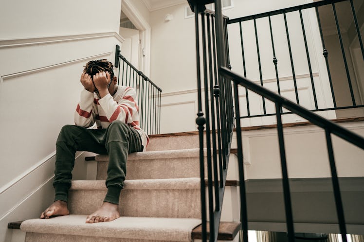 A sad boy grieving the loss of his dad sits on the stairs with his head in his hands.