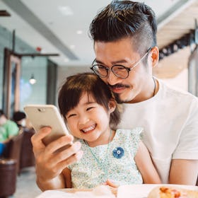 Asian dad and young daughter smiling for selfie in a diner