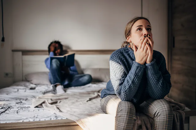 A woman sits on the end of the bed after an argument with her husband.