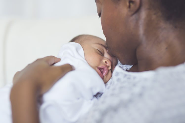 A Black mom in hospital scrubs holds her newborn to her chest.