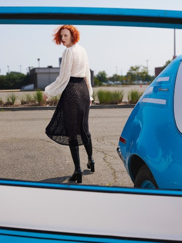 Model Karen Elson is wearing a black and white lace dress and knee high leather boots.