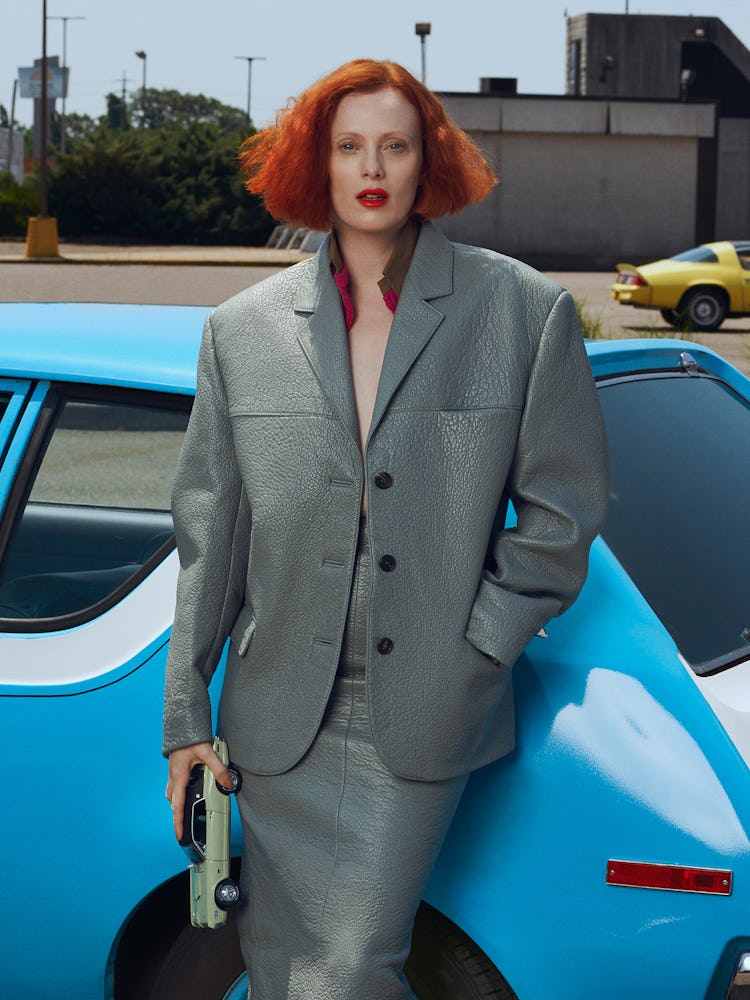 Model Karen Elson wears a gray leather jacket & skirt and is holding a green toy car.
