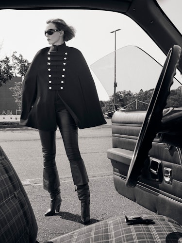 Model Karen Elson is wearing a black wool cape, sunglasses, leather pants, and leather boots.