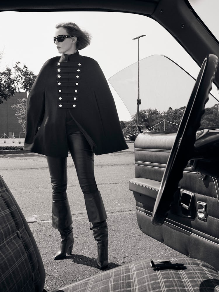Model Karen Elson is wearing a black wool cape, sunglasses, leather pants, and leather boots.