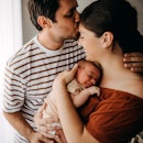 A dad kisses his wife on the forehead while she holds their newborn baby.