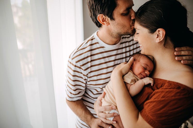 A dad kisses his wife on the forehead while she holds their newborn baby.