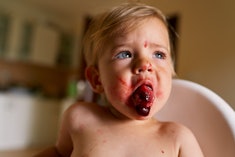 Toddler with messy face sits in a high chair and spits out a cherry, in a story explaining why your ...