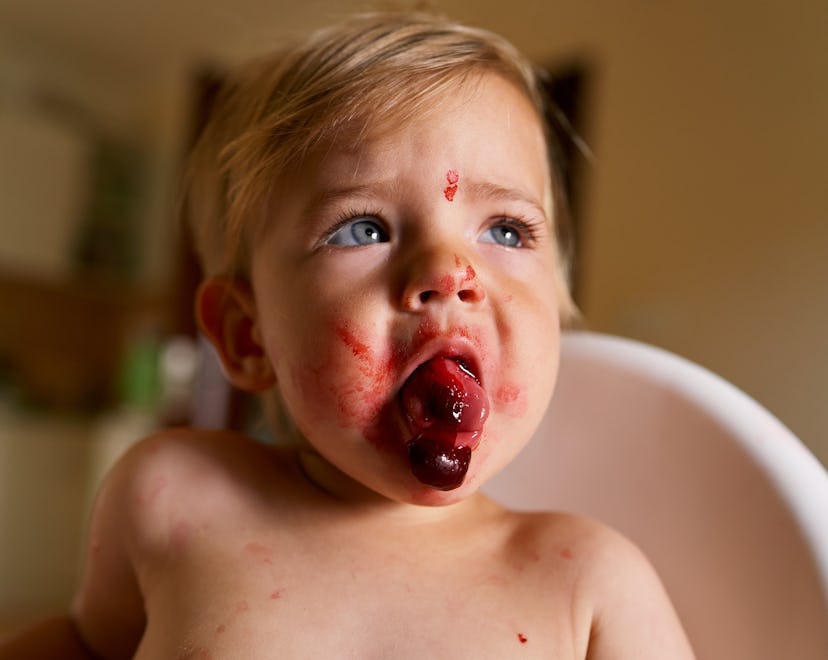 Toddler with messy face sits in a high chair and spits out a cherry, in a story explaining why your ...