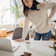 A woman clutches her lower back in pain as she gets up from her desk.