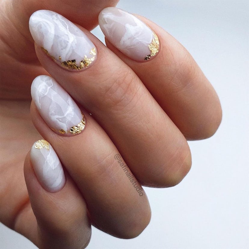 White marble nail art with gold leaf details on short almond nails are on-trend for 2024.